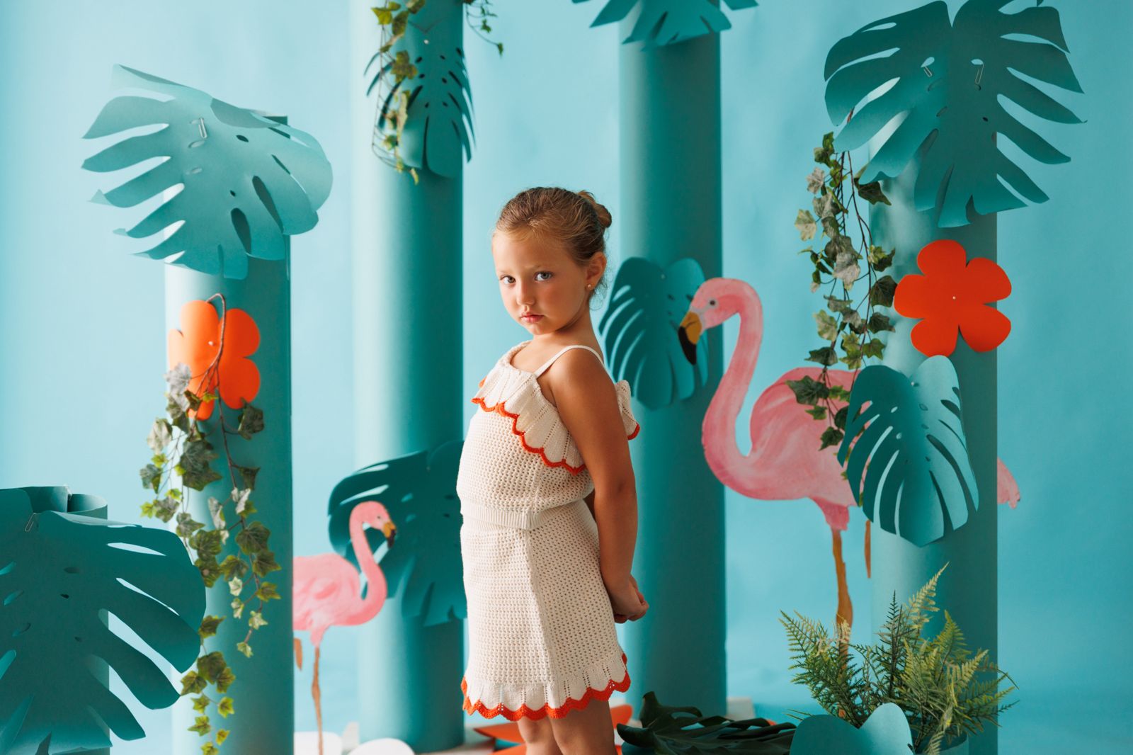 Niña posando en un escenario fotográfico infantil con temática de selva azul, flamencos rosas y hojas de monstera.
