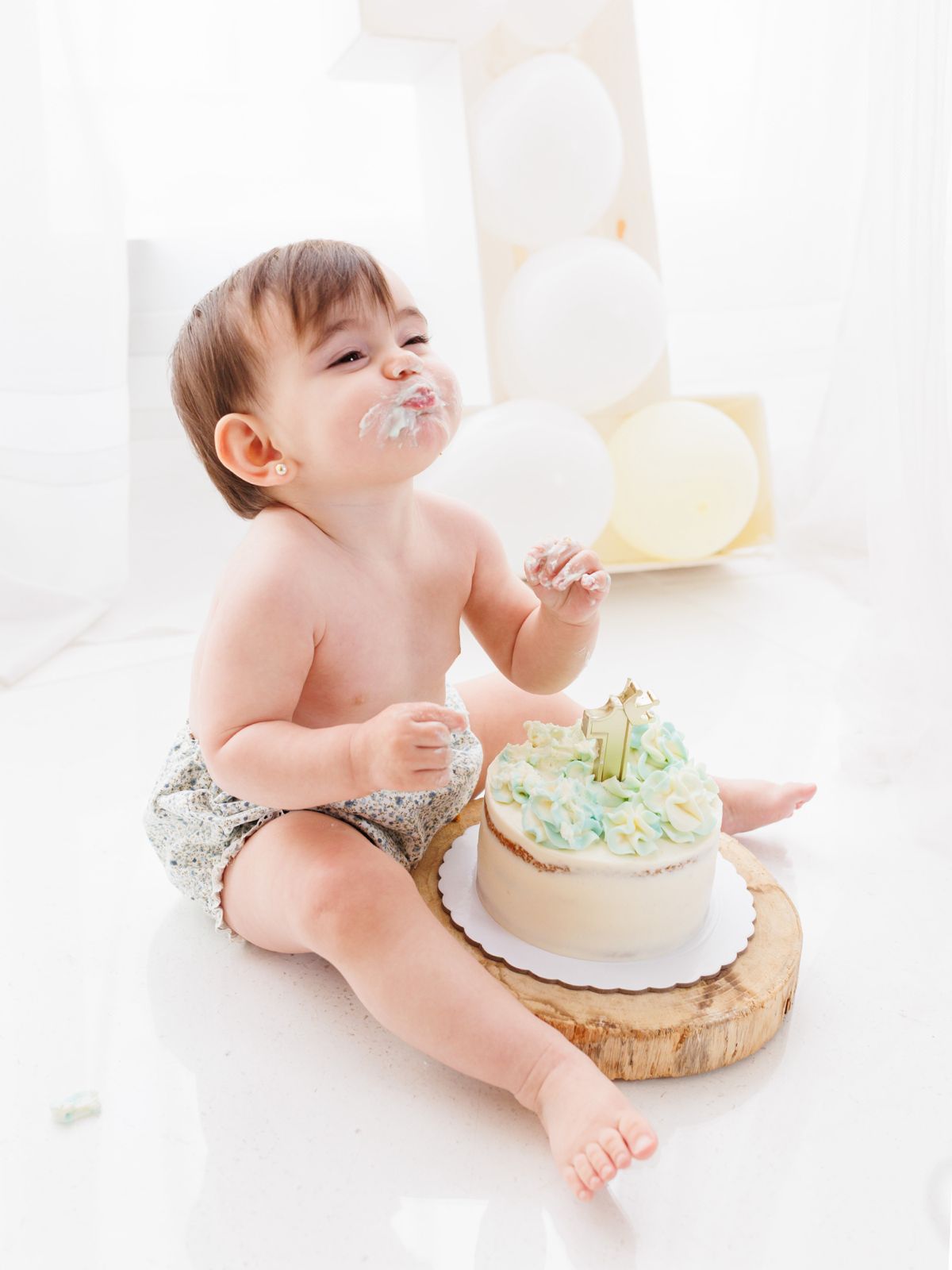 Bebé de un año sentado en el suelo con la cara manchada de crema disfrutando de su pastel de cumpleaños.